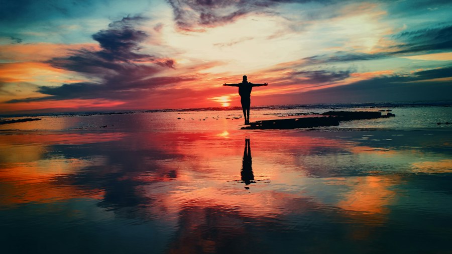 A person walking beside water under a colorful sky